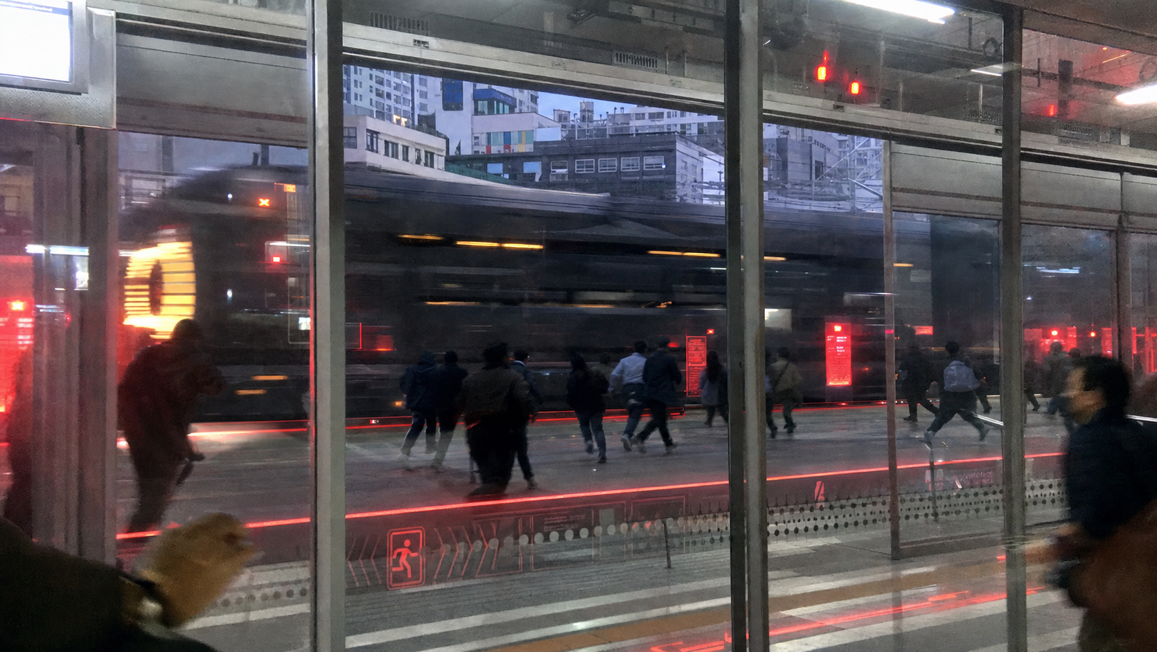 플랫폼 안전유리 너머로 시민들이 대피 동선으로 이동하는 광경, 반사된 도시 풍경 위로 RRT가 통과한다